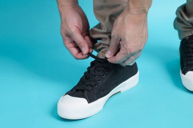 Erkek eli bağlayan spor ayakkabı bağı, mavi arka planda izole edilmiş.. 