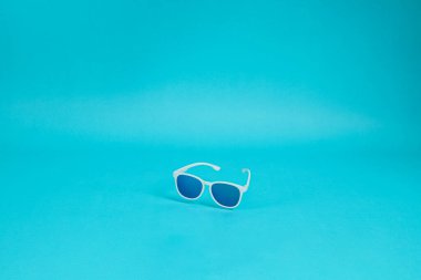 Mavi arkaplanda beyaz plastik çerçeveli modern güneş gözlüğü.