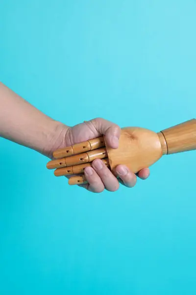 Hand of mannequin shake hands with human hand on isolated blue background. Symbol, teamwork.