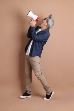 Asyalı bir adam izole edilmiş kahverengi arka planda bir megafon tutuyor.