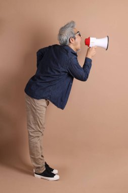 Asyalı bir adam izole edilmiş kahverengi arka planda bir megafon tutuyor.