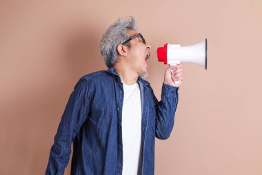 Asyalı bir adam izole edilmiş kahverengi arka planda bir megafon tutuyor.