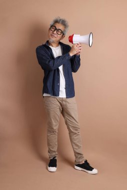 Asyalı bir adam izole edilmiş kahverengi arka planda bir megafon tutuyor.