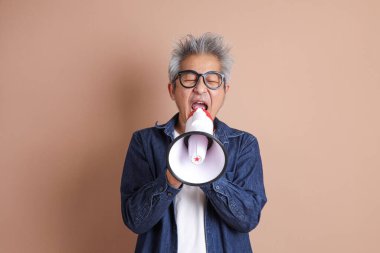 Asyalı bir adam izole edilmiş kahverengi arka planda bir megafon tutuyor.