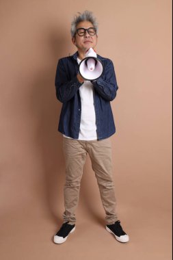 Asyalı bir adam izole edilmiş kahverengi arka planda bir megafon tutuyor.