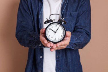 Asyalı adamın elinde mavi arka plan, zaman yönetimi ve denge için bir saat var.