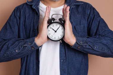 Asyalı adamın elinde mavi arka plan, zaman yönetimi ve denge için bir saat var.