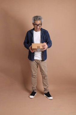 Asyalı adam bir kutu tutuyor, teslimat konsepti, alışveriş ya da iş, kahverengi arka plan