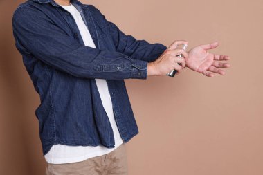 Asyalı adam kahverengi arka planda yalnız poz veriyor. Salgın koronavirüs 2019-ncov sarar covid-19 grip virüsü. Elinde antibakteriyel dezenfektanla şişeyi tutuyor..