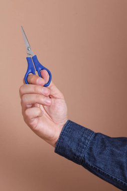 Kahverengi arka planda izole edilmiş Asyalı erkek eli makasına yakın çekim