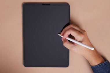 Adamın eli, kahverengi arka planda izole edilmiş boş tablete bir stil kalem ya da stilus kalem tutuyor. Yeni dijitalleştirici kalem. Siyah tablet dokunmatik ekran modeli.