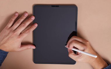 Adamın eli, kahverengi arka planda izole edilmiş boş tablete bir stil kalem ya da stilus kalem tutuyor. Yeni dijitalleştirici kalem. Siyah tablet dokunmatik ekran modeli.