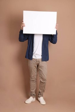 Elinde boş bir tuval tutan, gözlüklü, Asyalı, enerjik, üst düzey bir adam. Kahverengi arka planda, günlük kıyafetlerle izole edilmiş. Olgun adam, Asyalı adam. Yaşlı, stüdyo fotoğrafı. Çoklu duygular. 