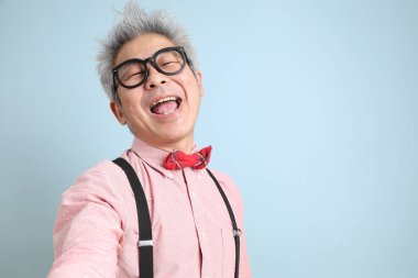 Asyalı, siyah pantolon askısı takmış, kırmızı fiyonklu, mavi arka planda izole edilmiş selfie çeken son sınıf öğrencisi. Sevgililer Günü