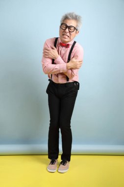 Asyalı, siyah pantolon askısı takan, kırmızı fiyonklu, mavi arka planda soğuk hissetme hareketi yapan son sınıf öğrencisi. Sevgililer Günü