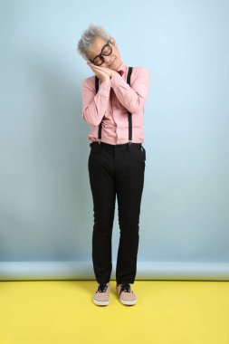 Asyalı, siyah pantolon askısı takmış, kırmızı pruvalı, mavi arka planda Uykucu işareti olan son sınıf öğrencisi. Sevgililer Günü