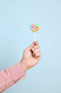 Mavi arka planda kalp şeklinde lolipop tutan kıdemli bir adamın eli. Sevgililer Günü, Kadınlar Günü, Tatlı Dişli