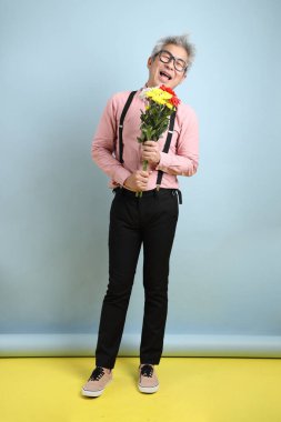 Asyalı siyah pantolon askısı ve kırmızı fiyonklu son sınıf öğrencisi mavi arka planda bir buket çiçek tutuyor. Sevgililer Günü, Kadınlar Günü, Doğum Günü