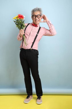 Asyalı siyah pantolon askısı ve kırmızı fiyonklu son sınıf öğrencisi mavi arka planda bir buket çiçek tutuyor. Sevgililer Günü, Kadınlar Günü, Doğum Günü