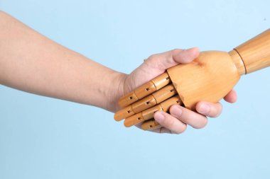 İzole edilmiş mavi arka planda insan eliyle tokalaşan bir manken eli. Sembol, takım çalışması.