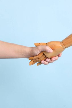 İzole edilmiş mavi arka planda insan eliyle tokalaşan bir manken eli. Sembol, takım çalışması.