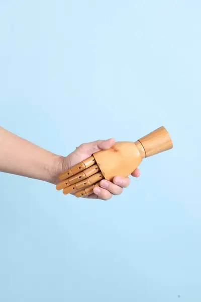 Hand of mannequin shake hands with human hand on isolated blue background. Symbol, teamwork.