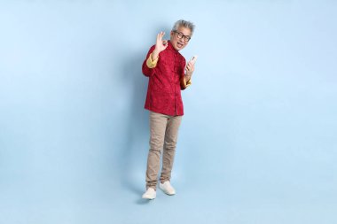 Yeni Çin yılın kutlu olsun. Asya 'nın enerjik kıdemli adamı kırmızı geleneksel Cheongsam Qipao ya da Changshan elbisesi giyiyor ve mavi arka planda cep telefonlarını izole ediyor..