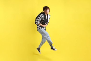 Okul çantasında Jump jesti taşıyan ekose gömlek giyen bir üniversite öğrencisi. Eğitim, yurtdışında eğitim, Z jenerasyonu, E-öğrenim. Ergen.