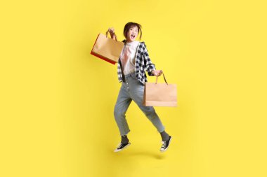 Okul çantasında atlama ve alışveriş çantası taşıyan ekose gömlek giyen bir üniversite öğrencisi. Eğitim, yurtdışında eğitim, Z jenerasyonu, E-öğrenim. Ergen.