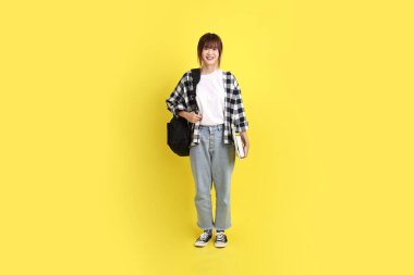 Okul çantası ve kitap taşıyarak ayakta duran ekose gömlek giyen bir üniversite öğrencisi. Eğitim, yurtdışında eğitim, Z jenerasyonu, E-öğrenim. Ergen.