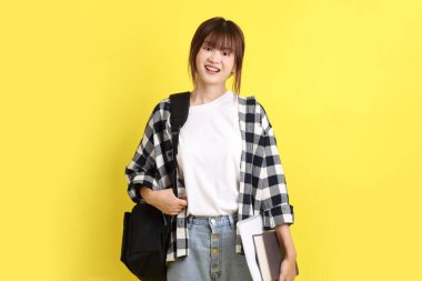 Okul çantası ve kitap taşıyarak ayakta duran ekose gömlek giyen bir üniversite öğrencisi. Eğitim, yurtdışında eğitim, Z jenerasyonu, E-öğrenim. Ergen.