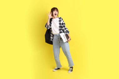 Okul çantası ve kitap taşırken ekose gömlek giyen bir üniversite öğrencisi sürpriz bir hareketle. Eğitim, yurtdışında eğitim, Z jenerasyonu, E-öğrenim. Ergen.