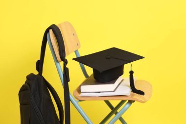 Okul kitaplarıyla, ders kitaplarıyla, sırt çantasıyla ve sarı arka planda izole edilmiş sınıf sandalyesindeki kırtasiye malzemeleriyle okul konseptine geri dönelim. Yurtdışında okumak, Z Geni, E-öğrenimi.