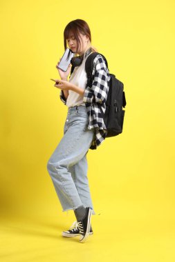 Ekose gömlek giyen Asyalı kız öğrenci okul çantası ve kulaklık taşıyor ve cep telefonlu kredi kartı taşıyor. Eğitim, yurtdışında öğrenim, Z Geni, E-öğrenim.