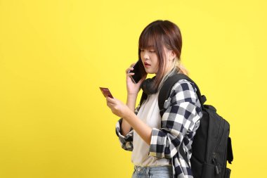 Ekose gömlek giyen Asyalı kız öğrenci okul çantası ve kulaklık taşıyor ve cep telefonlu kredi kartı taşıyor. Eğitim, yurtdışında öğrenim, Z Geni, E-öğrenim.