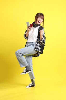 Ekose gömlek giyen Asyalı kız öğrenci okul çantası ve kulaklık taşıyor ve cep telefonlu kredi kartı taşıyor. Eğitim, yurtdışında öğrenim, Z Geni, E-öğrenim.