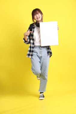 Ekose gömlek giyen Asyalı kız öğrenci okul çantası ve kulaklık taşıyor. Üzerinde boş tuval var. Eğitim, yurtdışında öğrenim, Z Geni, E-öğrenim.