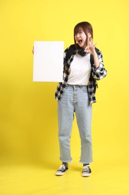 Ekose gömlek giyen Asyalı kız öğrenci okul çantası ve kulaklık taşıyor. Üzerinde boş tuval var. Eğitim, yurtdışında öğrenim, Z Geni, E-öğrenim.