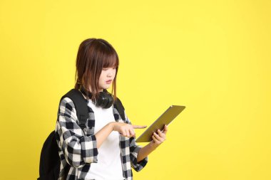 Ekose gömlek giyen Asyalı kız öğrenci okul çantası, ayakta durma ve tablet tutma hareketi taşıyor. Yurtdışında okumak, Z Geni, E-öğrenimi.