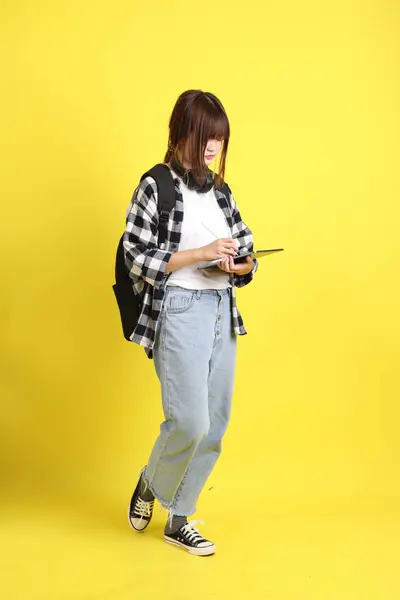 Ekose gömlek giyen Asyalı kız öğrenci okul çantası, ayakta durma ve tablet tutma hareketi taşıyor. Yurtdışında okumak, Z Geni, E-öğrenimi.