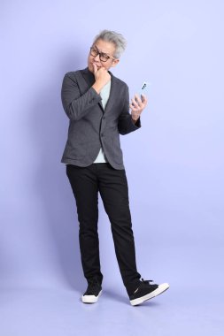 50 'li yılların Asyalı kıdemli iş adamı. Gözlüklü, resmi giyinmiş. Mor arka planda izole edilmiş cep telefonu bulundurma jesti.. 