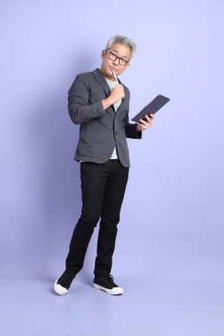 50 'li yılların Asyalı kıdemli iş adamı. Gözlüklü, resmi giyinmiş. Mor arka planda izole tablet tutmanın jesti.. 