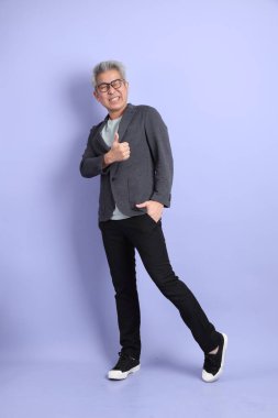 50 'li yılların Asyalı kıdemli iş adamı, gözlüklü, resmi kıyafetli, mor arka planda izole edilmiş baş parmak hareketleriyle.. 