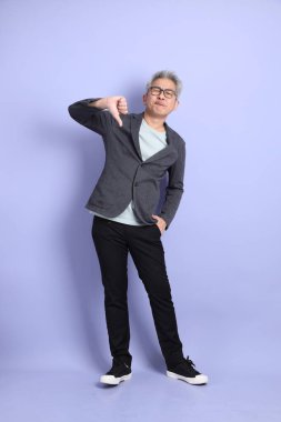 50 'lerin Asyalı kıdemli iş adamı, gözlüklü, resmi kıyafetli, mor arka planda izole edilmiş baş parmak hareketleriyle.. 