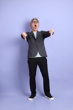 50 'lerin Asyalı kıdemli iş adamı, gözlüklü, resmi kıyafetli, mor arka planda izole edilmiş baş parmak hareketleriyle.. 