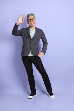 50 'lerin Asyalı kıdemli iş adamı, gözlüklü, resmi giyinmiş, iyi niyetli ya da mor arka planda izole edilmiş.. 