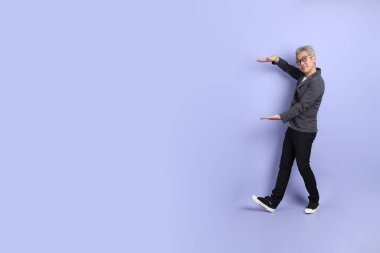 50 'li yılların Asyalı kıdemli iş adamı, gözlüklü, resmi giyinmiş. Mor arka planda büyük ve büyük boy işareti gösteren küçük miktarlarda bir jest yapıyor.. 