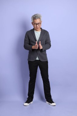 50 'li yılların Asyalı kıdemli iş adamı, gözlüklü, resmi giyinmiş. Mor arka planda büyük ve büyük boy işareti gösteren küçük miktarlarda bir jest yapıyor.. 