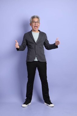 50 'li yılların Asyalı kıdemli iş adamı, gözlüklü, resmi giyinmiş. Mor arka planda büyük ve büyük boy işareti gösteren küçük miktarlarda bir jest yapıyor.. 