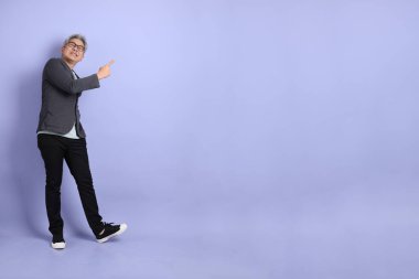 50 'li yılların Asyalı kıdemli iş adamı. Gözlüklü, resmi giyinmiş. Mor arka planda izole edilmiş bir yere işaret ediyor.. 